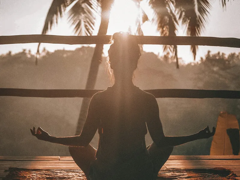 Personne en méditation, de dos, face au soleil couchant